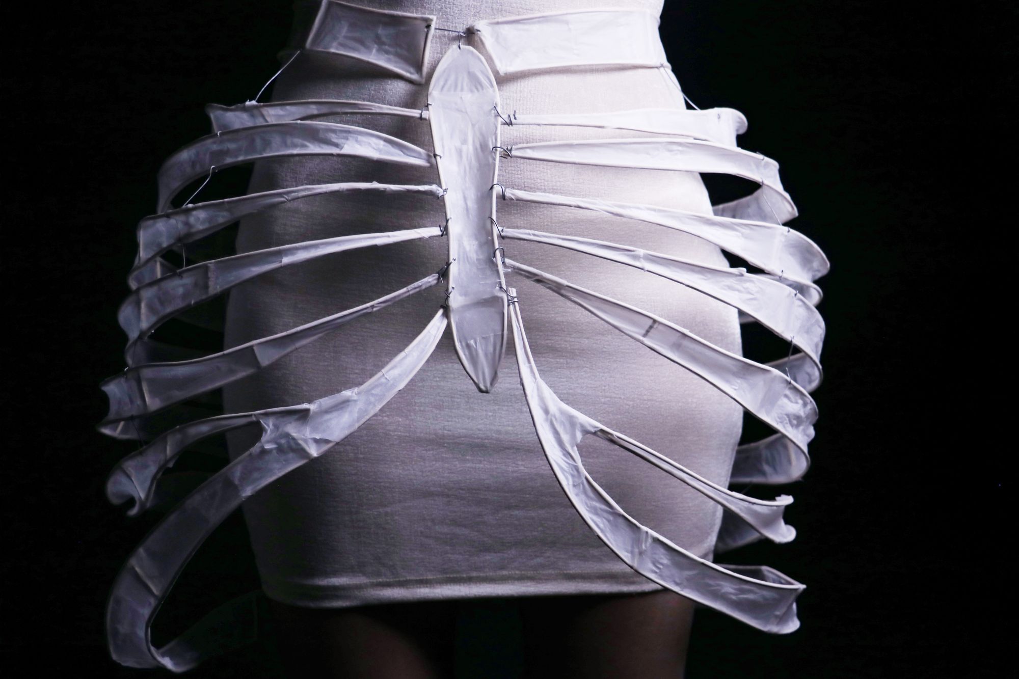 Close-up of the back of the dress, highlighting a skeletal, ribcage-inspired design with translucent curved bands and a central spine-like seam running vertically down a fitted cream skirt.